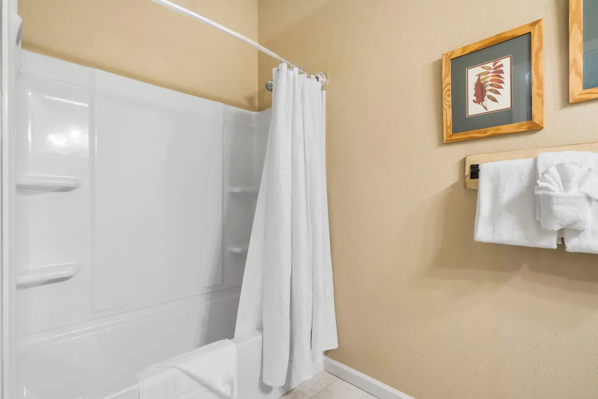 A serene bathroom scene with a bathtub, soft towels, shower curtain, and framed artwork. The clean and calm setting is perfect for unwinding after a long day.