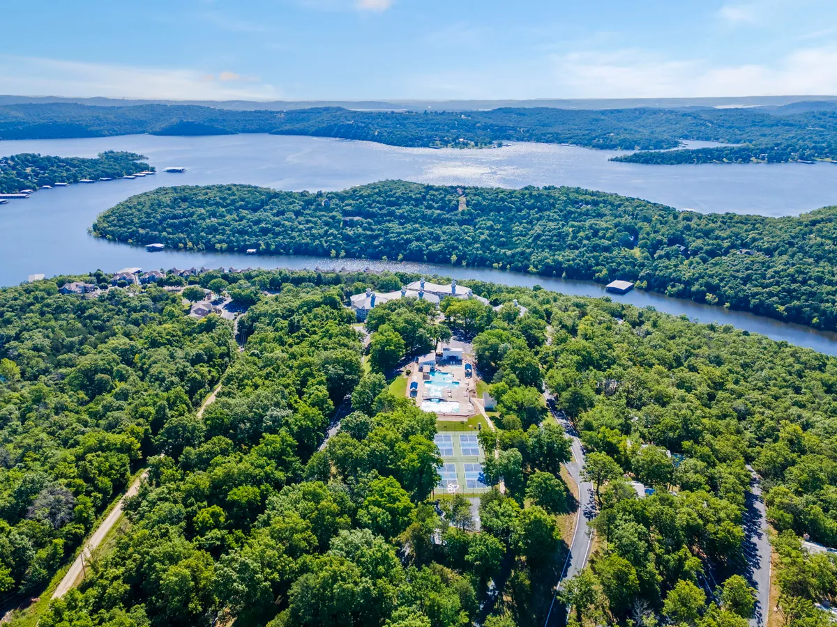 A sweeping view of Table Rock Lake framed by verdant greenery, with a swimming pool and tennis courts in the foreground. The scene blends water-based activities with on-site resort amenities, highlighting both the natural setting and recreational options.