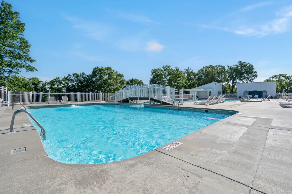 A sparkling swimming pool with a bridge and lounge chairs shaded by trees, inviting guests to relax or gather with friends. The lush landscaping and soft lighting suggest a resort-like environment ideal for leisure.