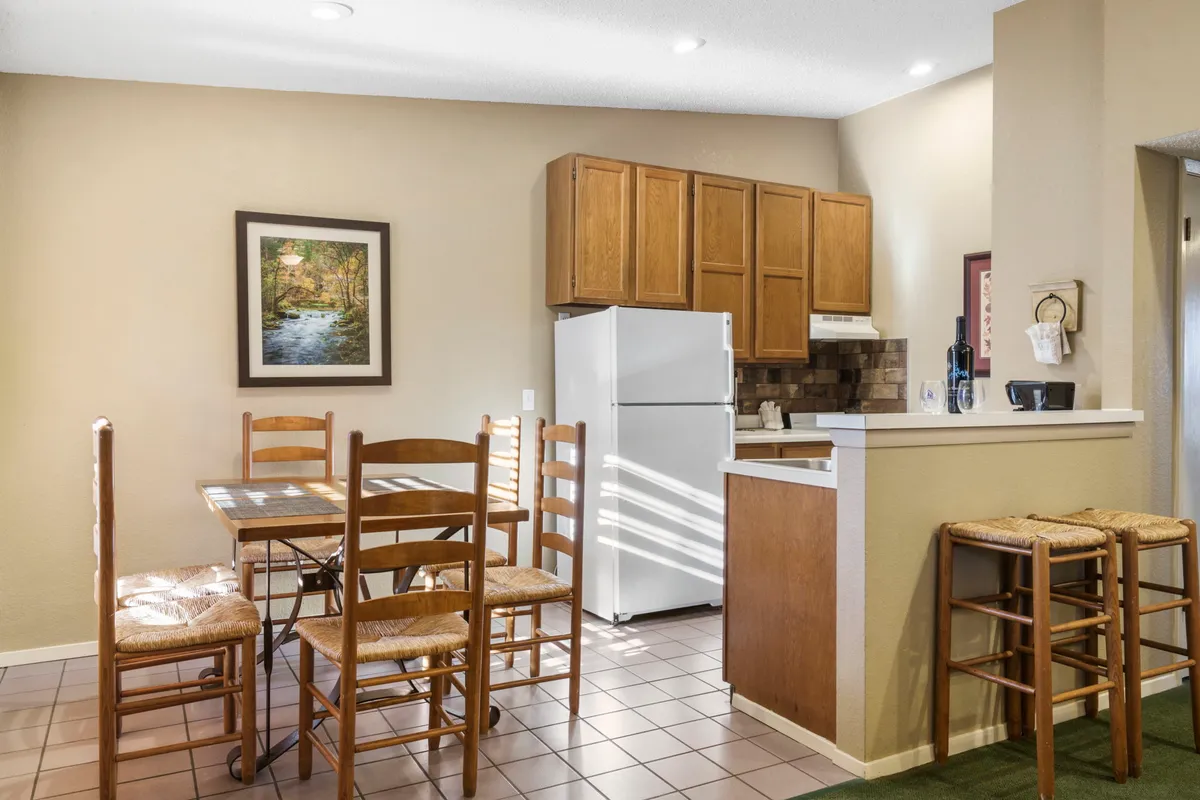 A view of a dining area with a wooden table, framed artwork on the wall, and a kitchen counter in the background. The space is set for casual family meals and gatherings, with soft lighting accentuating the cozy ambiance.