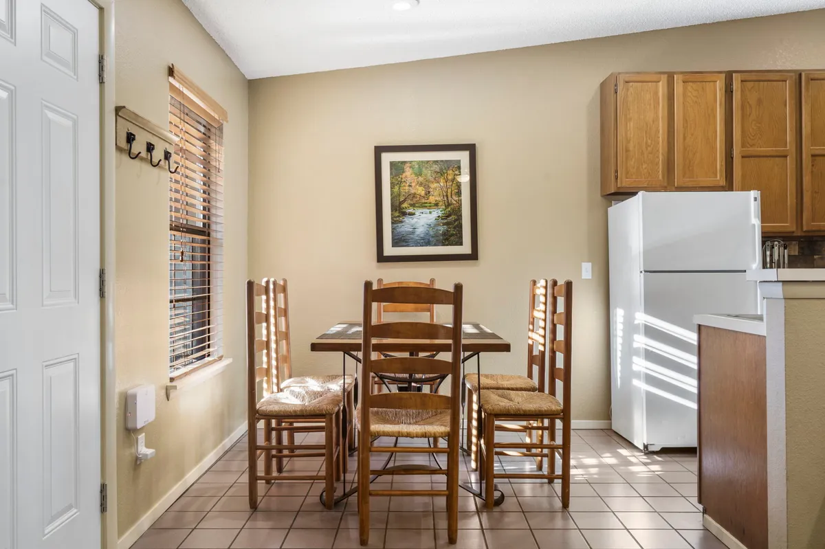 Inviting dining area with a dining table set for family meals, framed artwork on the wall, and a refrigerator in view. The scene is cozy and ideal for gathering, eating, and conversation.