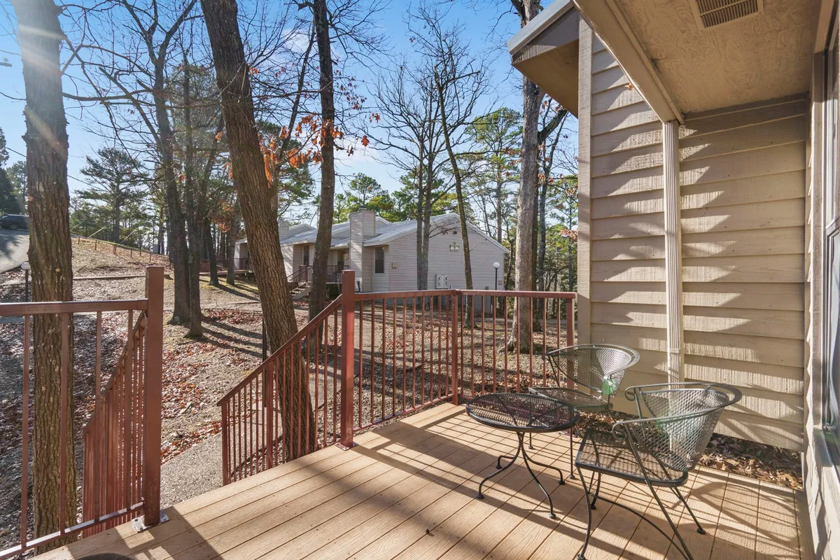 A relaxed exterior view featuring a deck with chairs set among tall shade trees, with a pathway leading off into the woods. The scene exudes tranquility and offers a sense of privacy and direct connection to nature—ideal for pet owners seeking outdoor relaxation and easy access to walking areas.