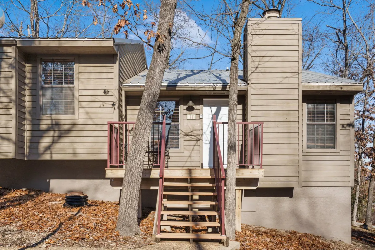 The inviting exterior entrance of a cabin with wood steps, a prominent front door, and a stone chimney, all surrounded by trees. The porch area suggests a welcoming atmosphere, with easy transitions from indoor comfort to outdoor adventure—important for pet families.