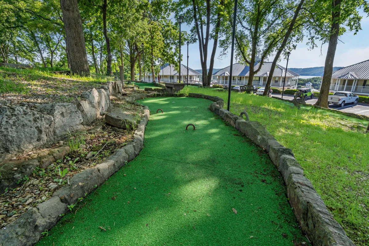 A vibrant mini-golf course surrounded by natural stone borders and lush, well-manicured grass. Trees in the background and the inviting putting greens create a playful and family-friendly atmosphere.