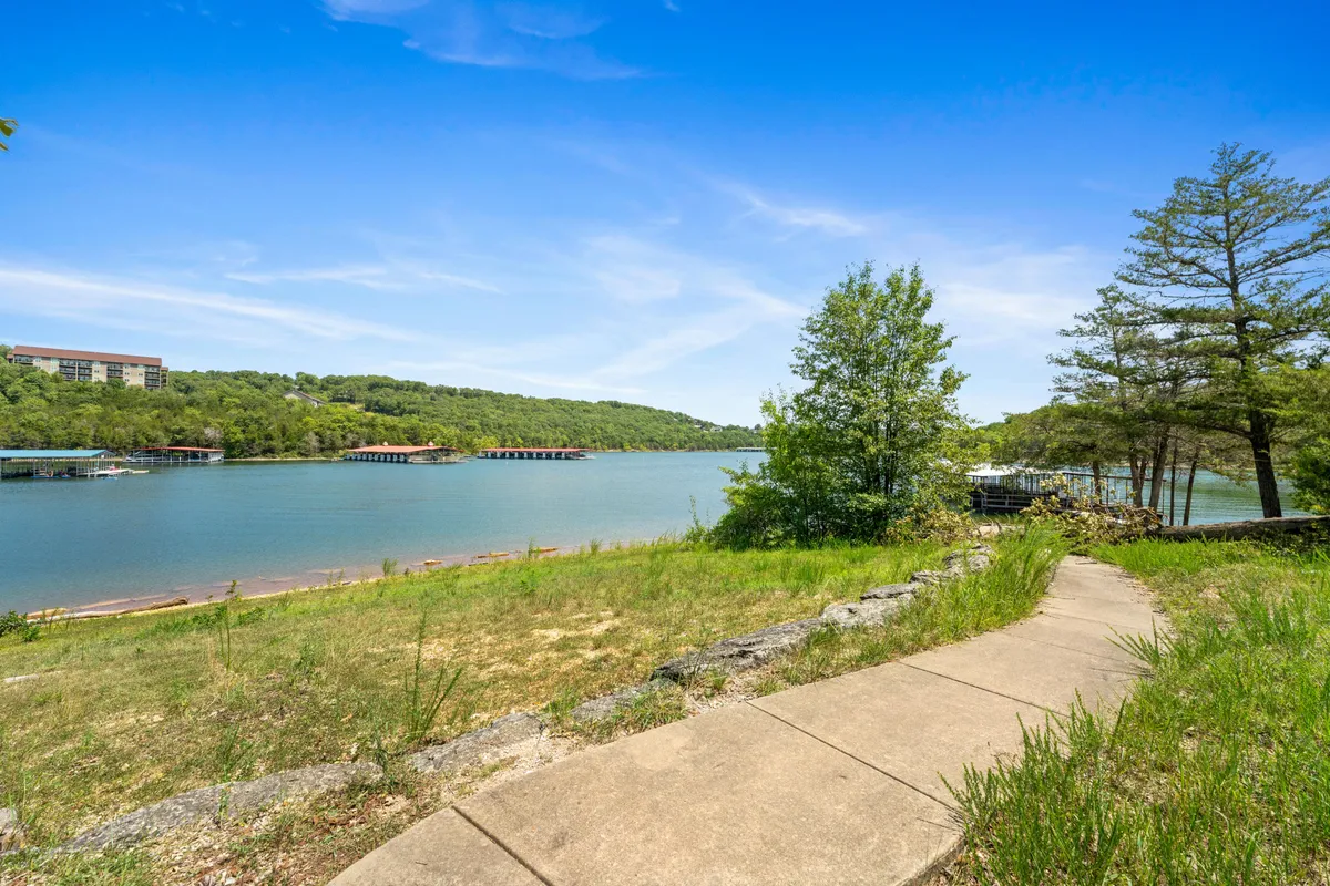 A scenic view of a pathway winding through trees toward the sparkling lake, set against rolling hills. The natural setting invites exploration, walking, and outdoor family adventures, evoking a sense of tranquility and discovery.